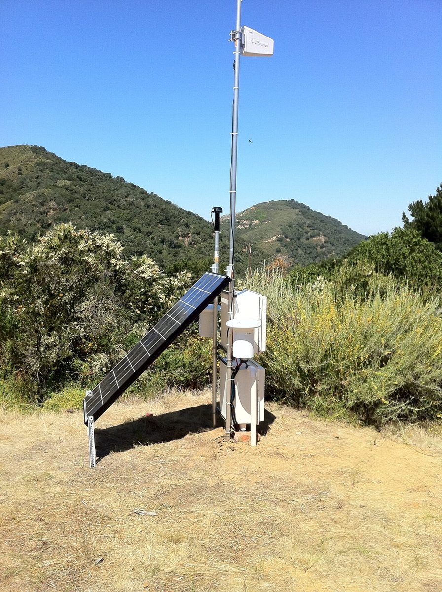A QuakeFinder magnetometer station: a solar panel and instrument enclosures on a mast, on a grassy California hillside